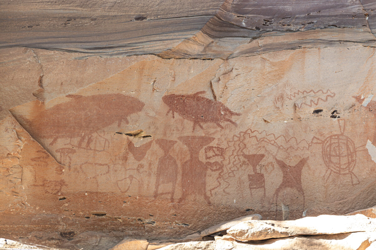Red-brown painted figures and line patterns on a pale rock surface at Pha Taem.
